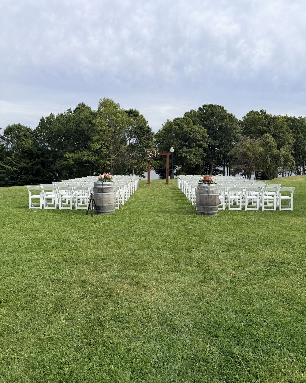 Ceremony chairs, wine barrels and a wooden arbor on the lawn at Colloca Estate Winery, with Little Sodus Bay behind