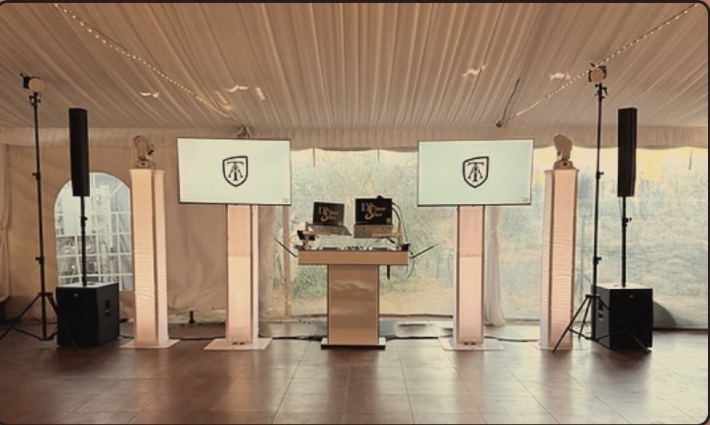 The same booth setup with the TV add-on: two large monogrammed screens on stands either side of the booth, under a tent
