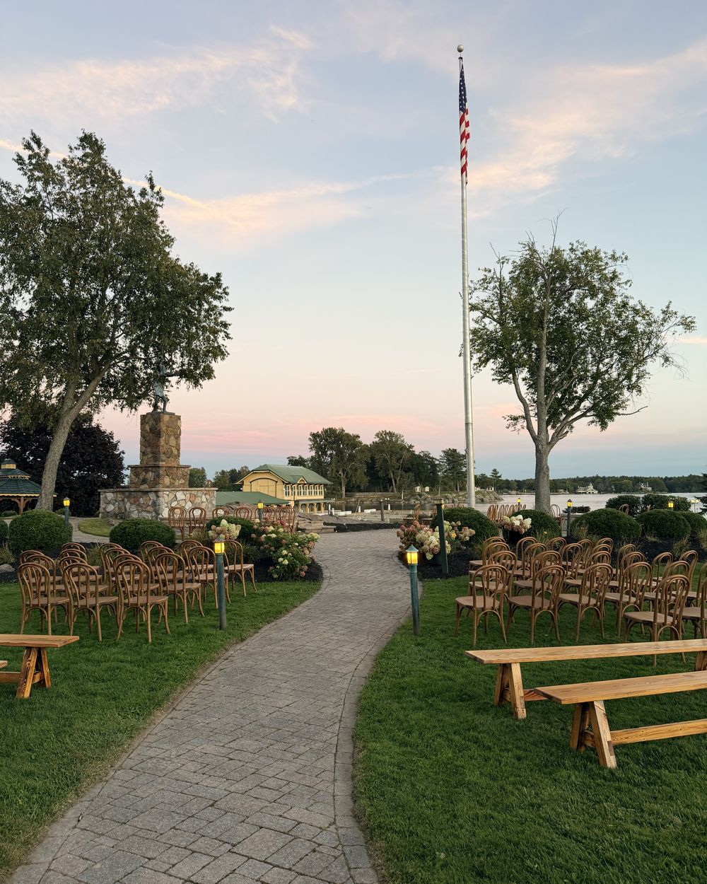 The ceremony aisle at the Thousand Islands Club running toward the stone monument, the boathouse and the St. Lawrence River at sunset